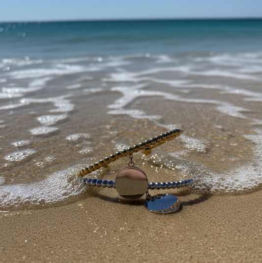 Bracelet with a shine charm to be engraved on a sandy beach with ocean waves.